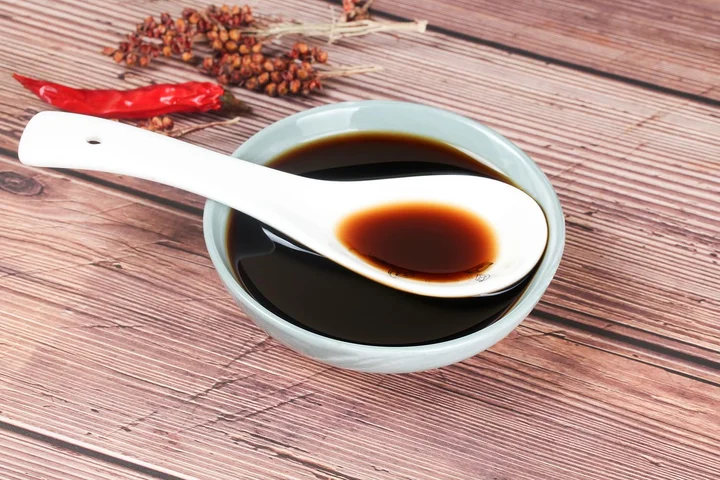 A spoon of dark vinegar resting over a blue dipping bowl